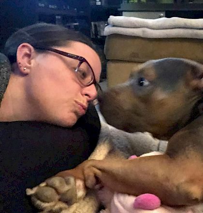A person lying close to a small dog, they appear to be napping or cuddling on a bed.