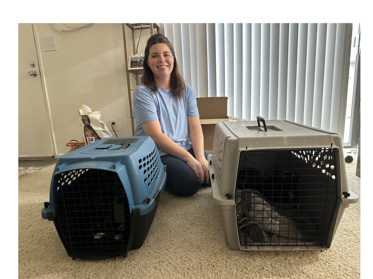 A smiling woman sits on the floor with two pet carriers&mdash;one blue and one gray&mdash;each containing a pet, in a bright room.