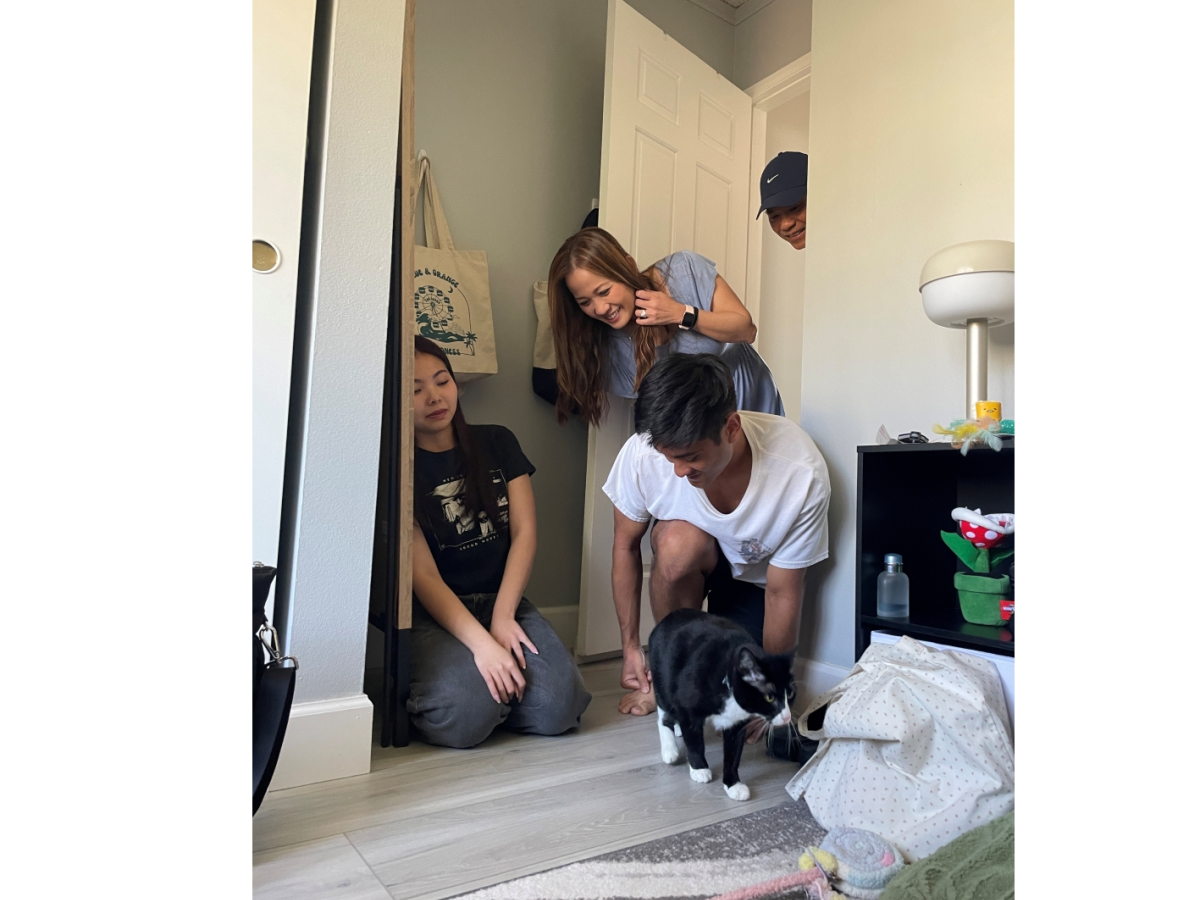 A group of four young people and a small dog gather in a doorway, smiling and posing playfully, inside a cozy room.