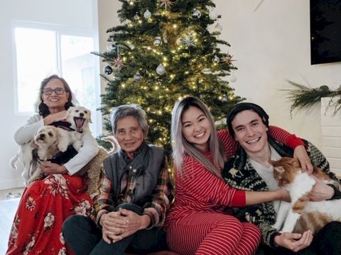 A cozy family holiday scene: five people on a sofa by a decorated Christmas tree, smiling with a dog, festive vibes, indoors.